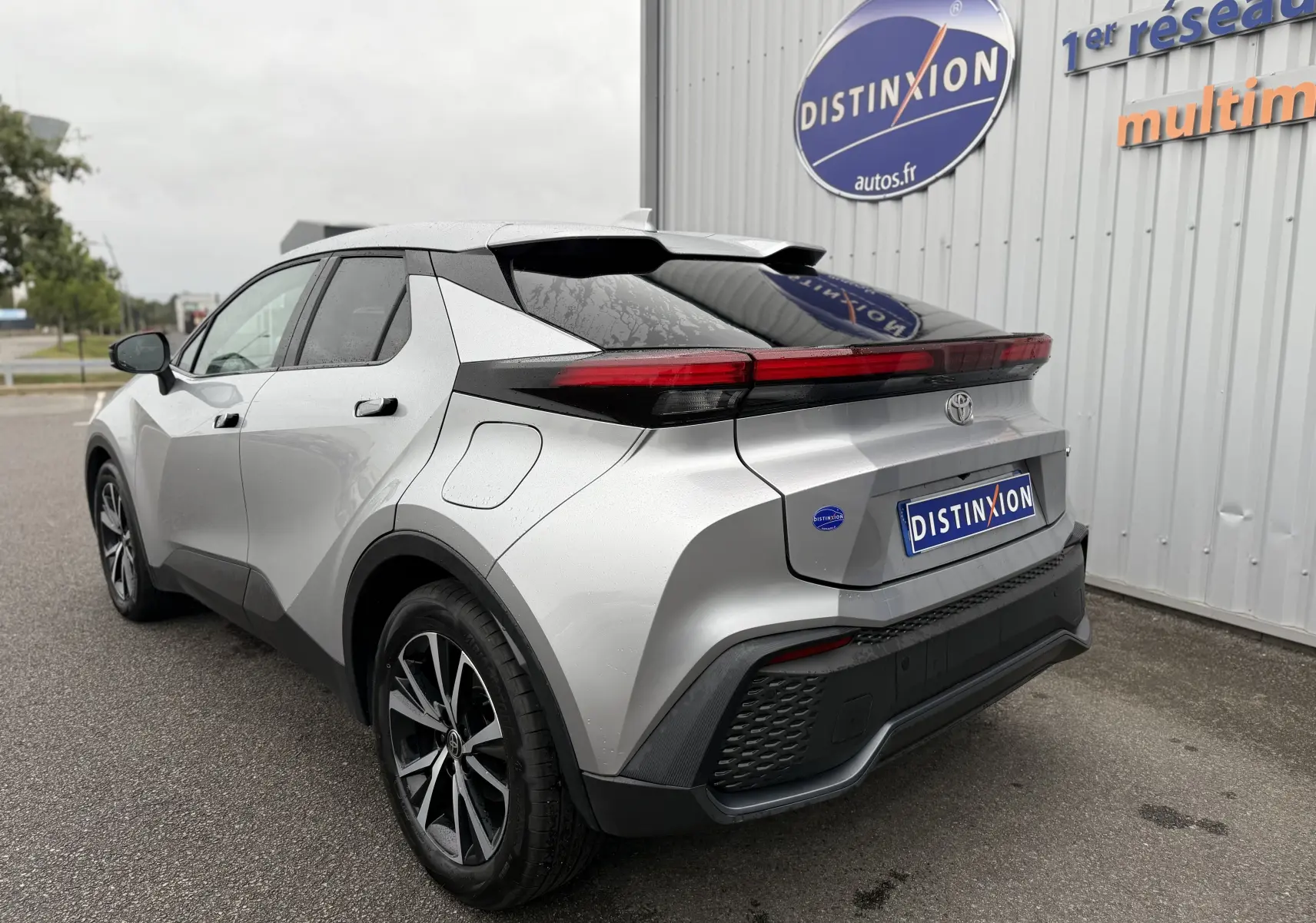 Vue 3/4 arrière gauche du Toyota C-HR Hybride gris 2024 avec feux arrière LED et jantes biton noir.