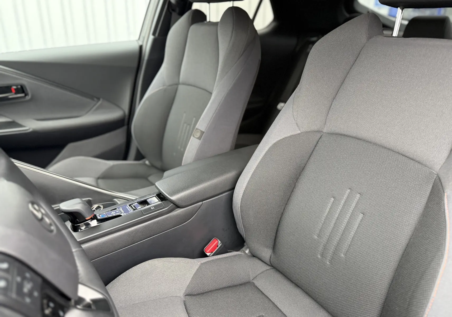 Vue intérieure rapprochée des sièges avant gris du Toyota C-HR Hybride 2024, avec console centrale et levier de vitesses visible.