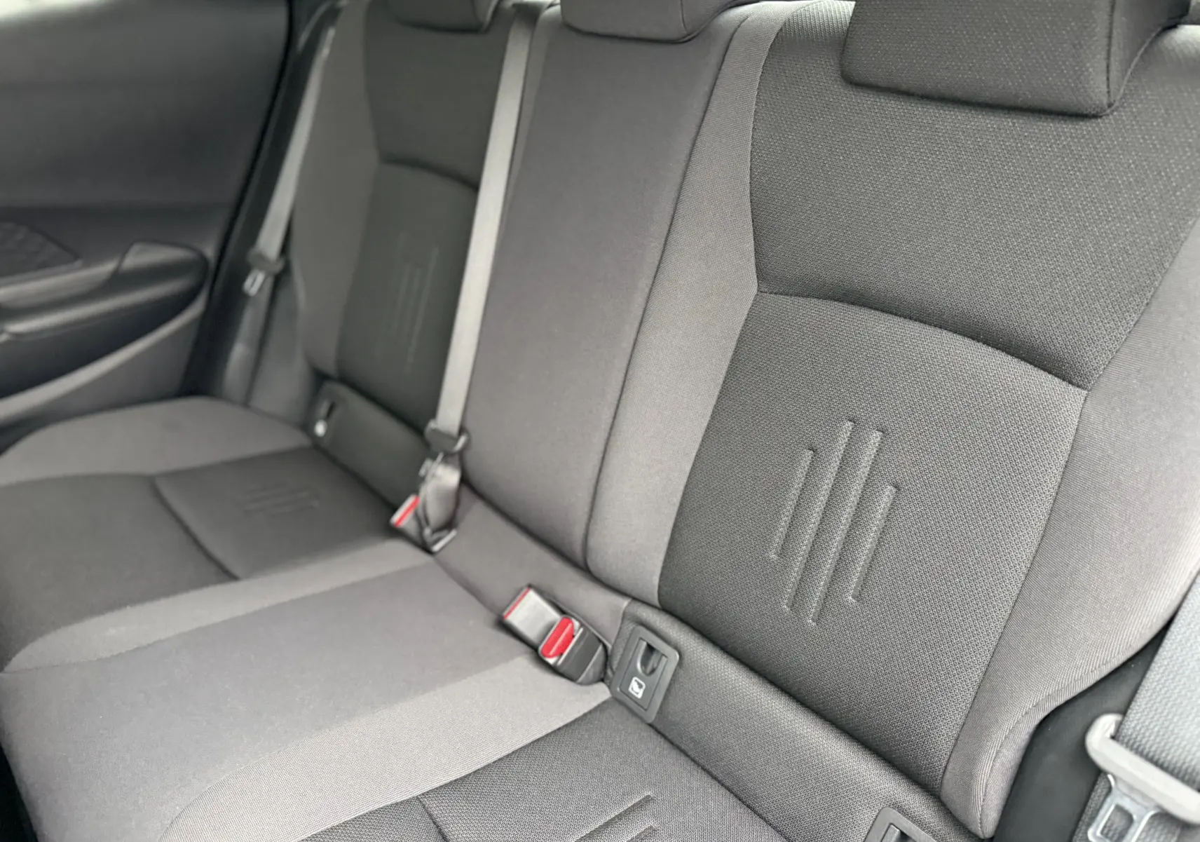 Vue rapprochée des sièges arrière gris du Toyota C-HR Hybride 2024, montrant les ceintures et les textures du tissu.