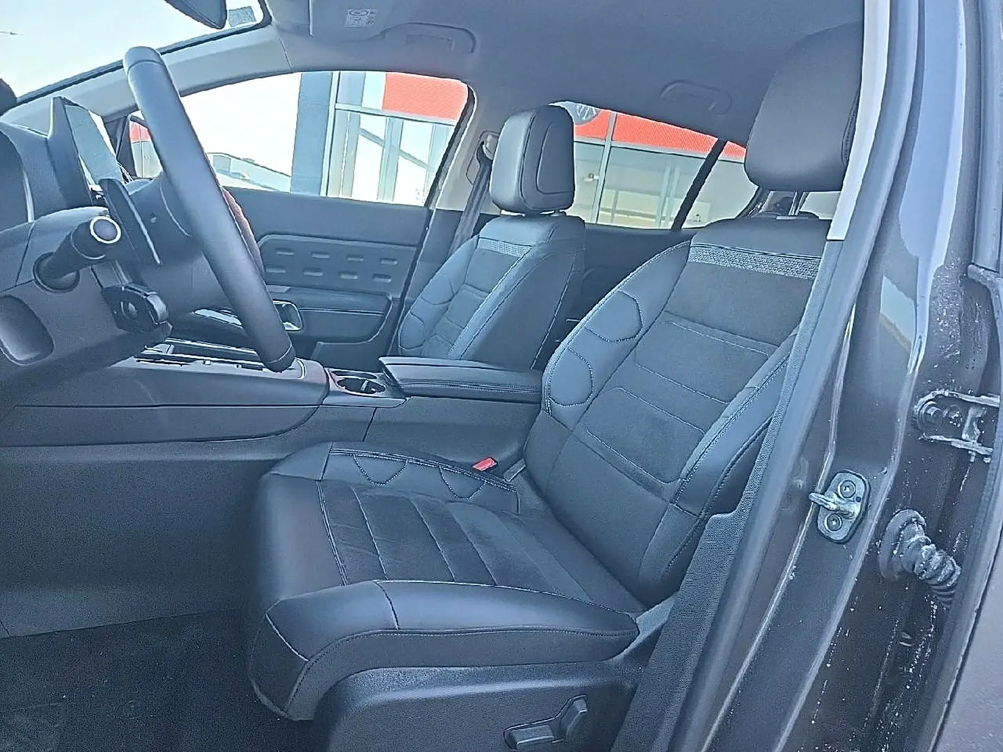 Vue intérieure côté conducteur du Citroën C5 Aircross gris platinium 2024, sièges avant en cuir noir avec accoudoir central.