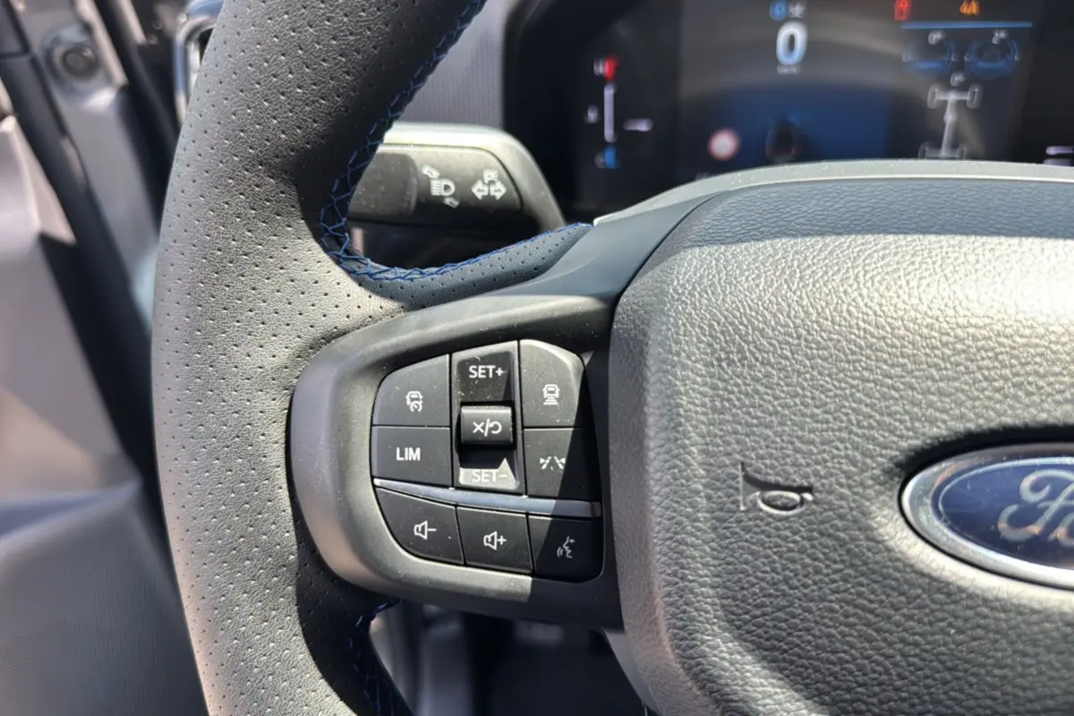 Gros plan sur le volant cuir perforé du Ford Ranger gris carbone, avec commandes multifonctions et logo Ford visible.