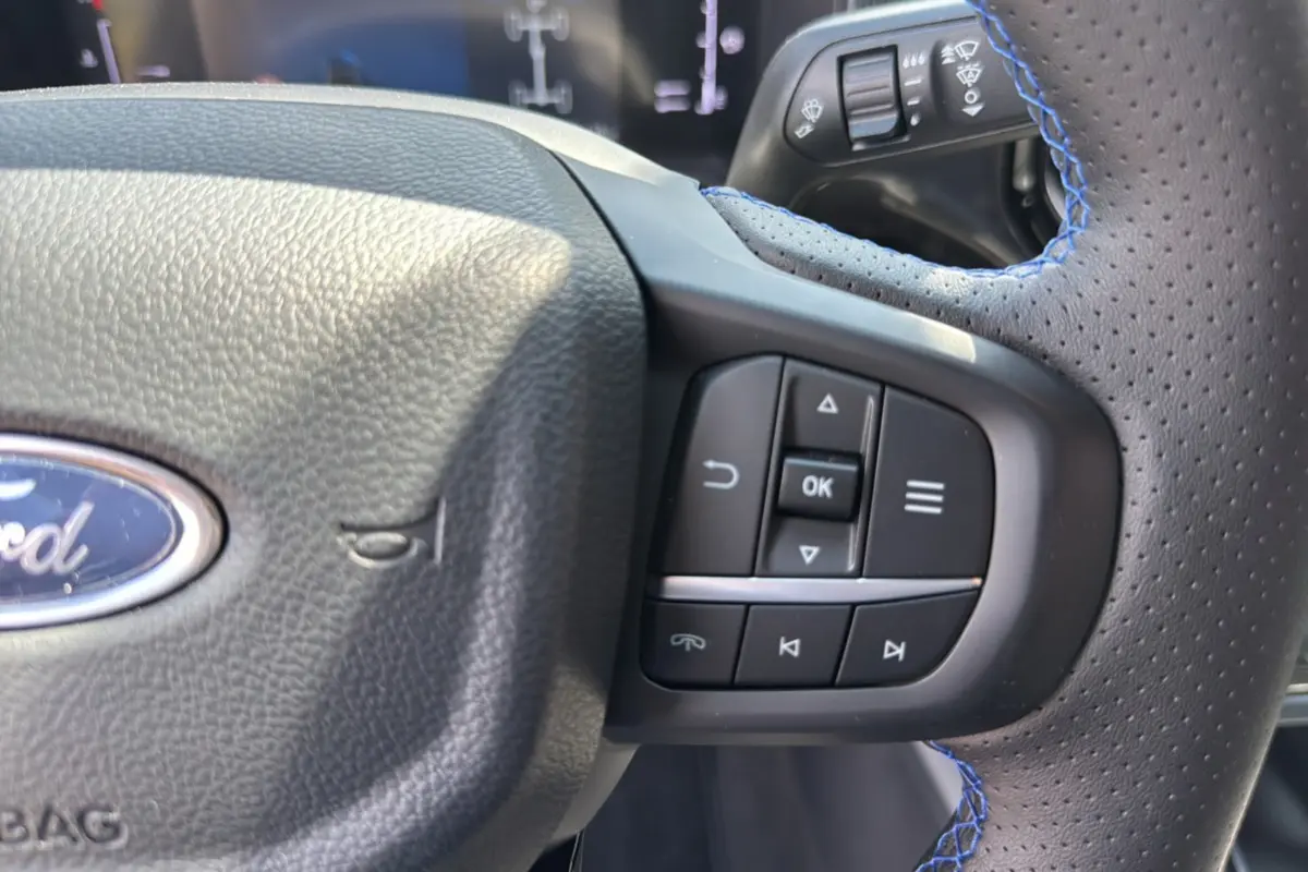 Gros plan sur le volant cuir perforé avec surpiqûres bleues du Ford Ranger gris carbone, montrant les commandes multifonctions.