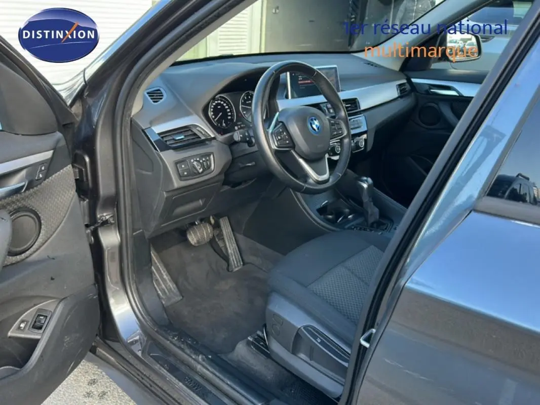 Intérieur côté conducteur d’un BMW X1 gris foncé 2022, volant sport et tableau de bord visible en lumière naturelle.