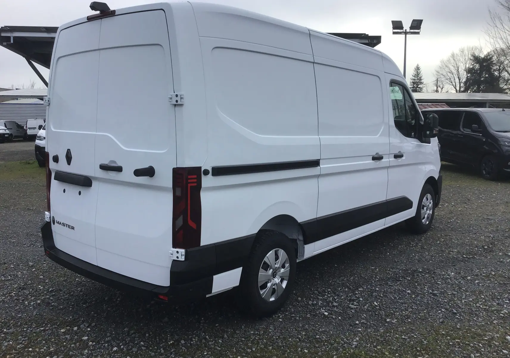 Vue 3/4 arrière droite d’un Renault Master blanc, fourgon utilitaire avec feux arrière verticaux et protections noires sur les flancs.