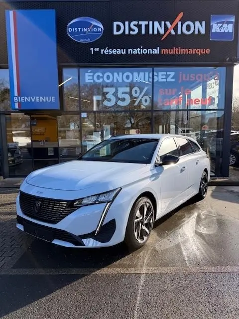 Peugeot 308 Hybrid blanc vue 3/4 avant droit, avec calandre noire et feux LED distinctifs, devant un showroom.