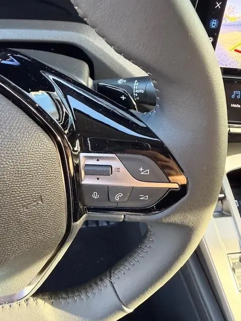 Gros plan sur les commandes multifonctions noires et argent du volant cuir de la Peugeot 308 Hybrid 145 e-DCS6 Allure blanche.
