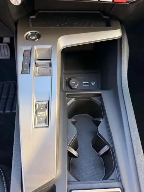 Vue rapprochée de la console centrale grise de la Peugeot 308 Hybrid 145 e-DCS6 Allure avec boutons de sélection et porte-gobelets.
