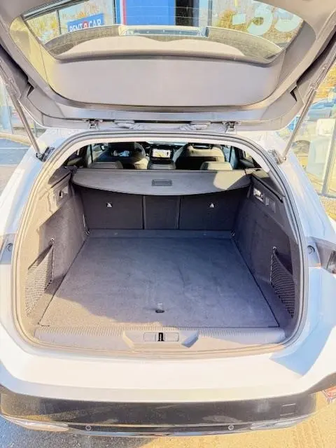 Vue arrière du coffre ouvert d'une Peugeot 308 Hybrid 145 e-DCS6 Allure blanche, montrant l'espace de chargement et la plage arrière.