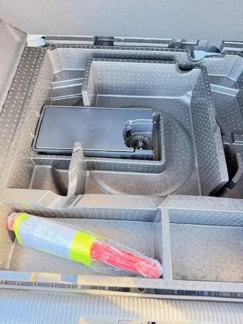 Vue rapprochée du rangement sous le plancher du coffre de la Peugeot 308 Hybrid 145 e-DCS6 Allure blanche, avec équipement de sécurité visible.