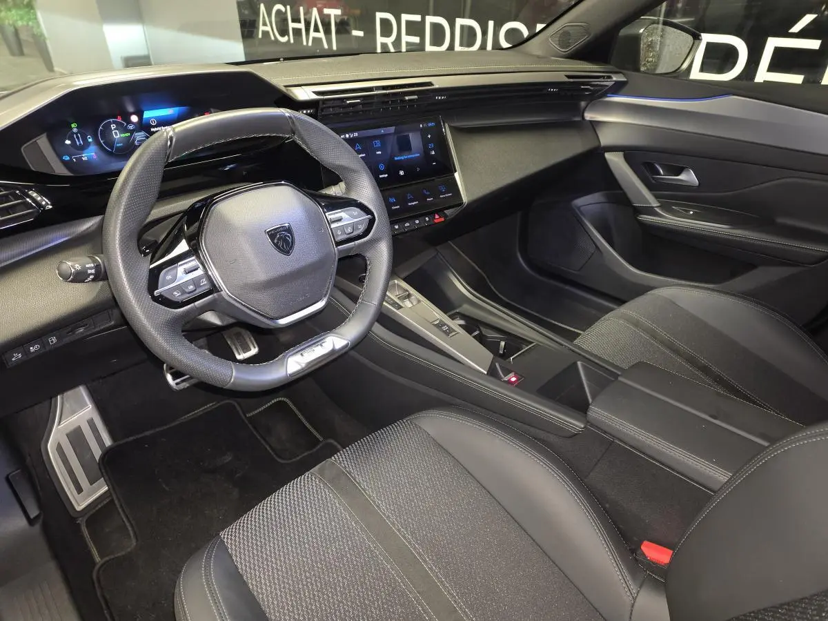 Vue intérieure côté conducteur de la Peugeot 408 GT 2025, tableau de bord noir avec volant cuir perforé et écran tactile central.