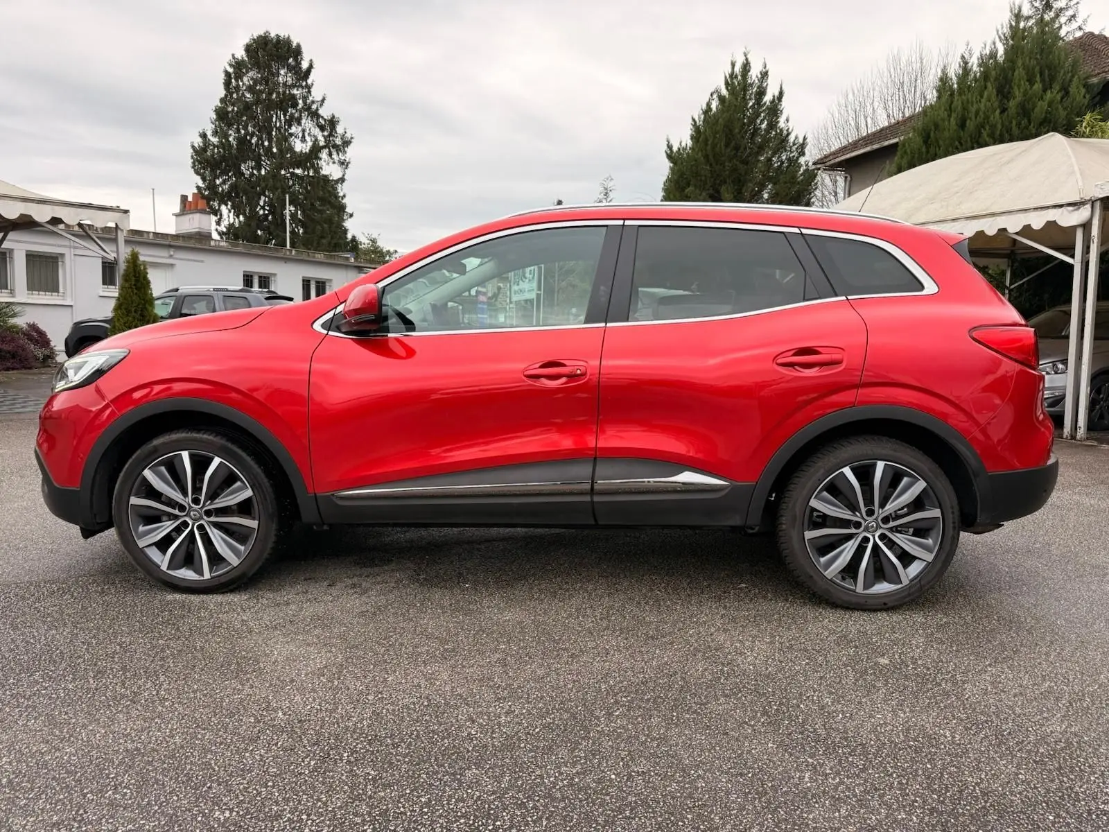 Vue de profil côté gauche d'un Renault Kadjar rouge flamme avec jantes alliage bicolores et protections noires basses.