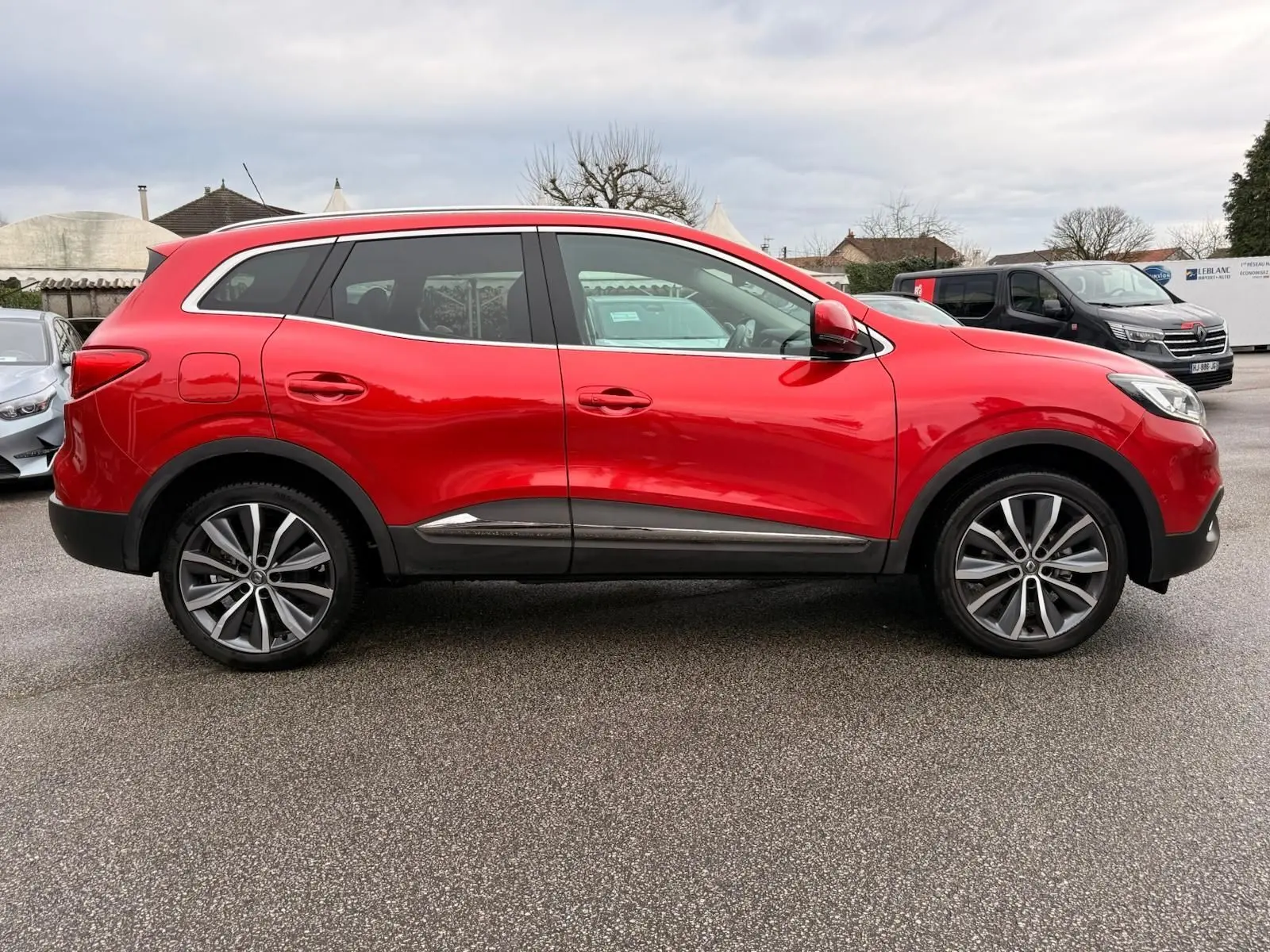Vue de profil côté gauche d'un Renault Kadjar rouge flamme avec jantes alliage bicolores et vitres teintées.