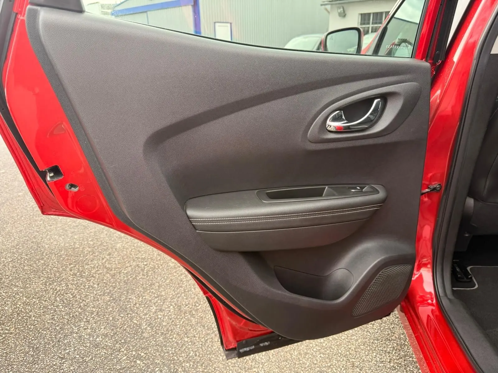 Vue rapprochée de la porte arrière gauche rouge flamme d’un Renault Kadjar 2016 avec garniture noire et poignée chromée.