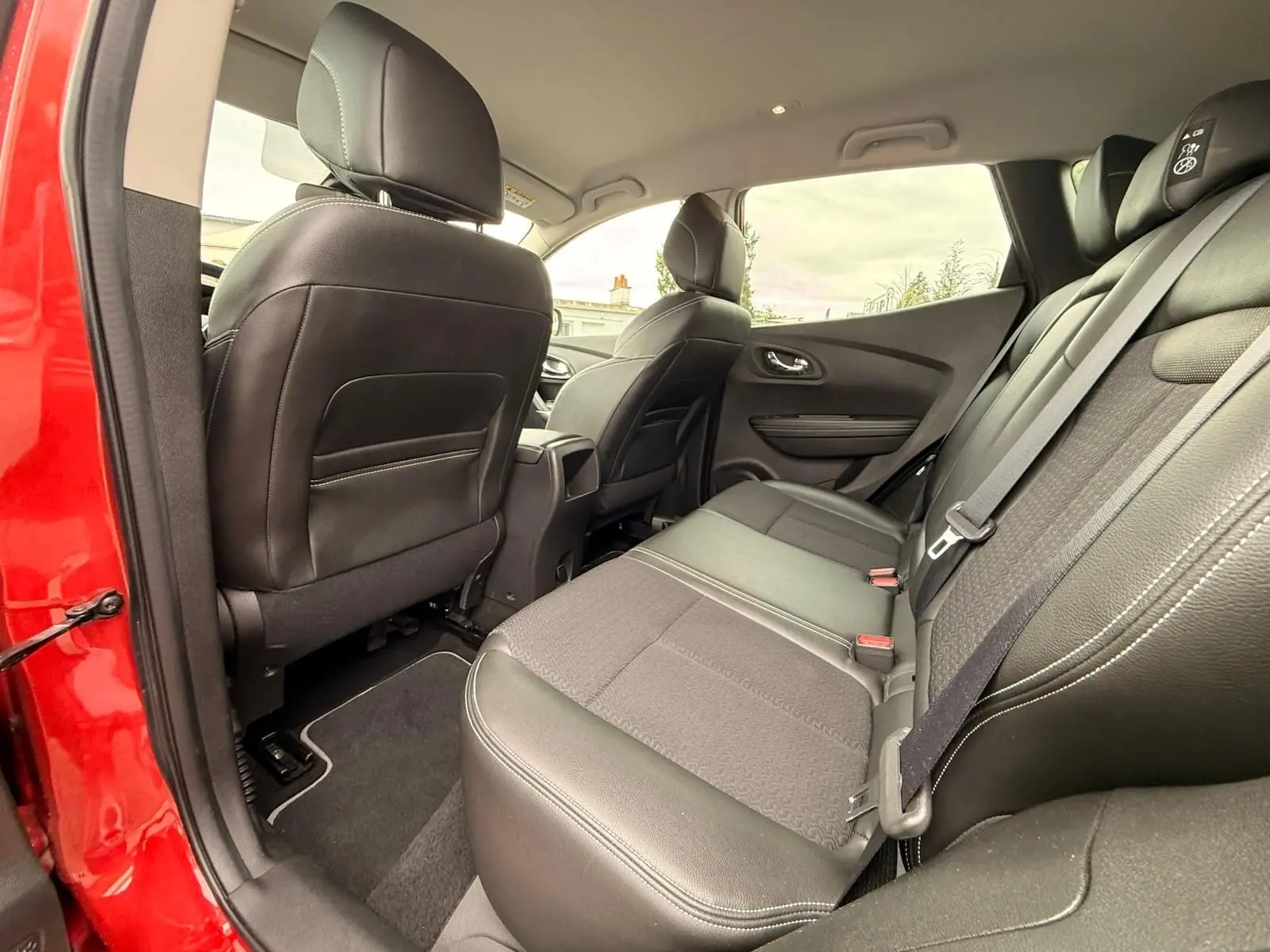 Vue intérieure arrière côté gauche du Renault Kadjar rouge flamme, sièges arrière en cuir noir et tissu gris.