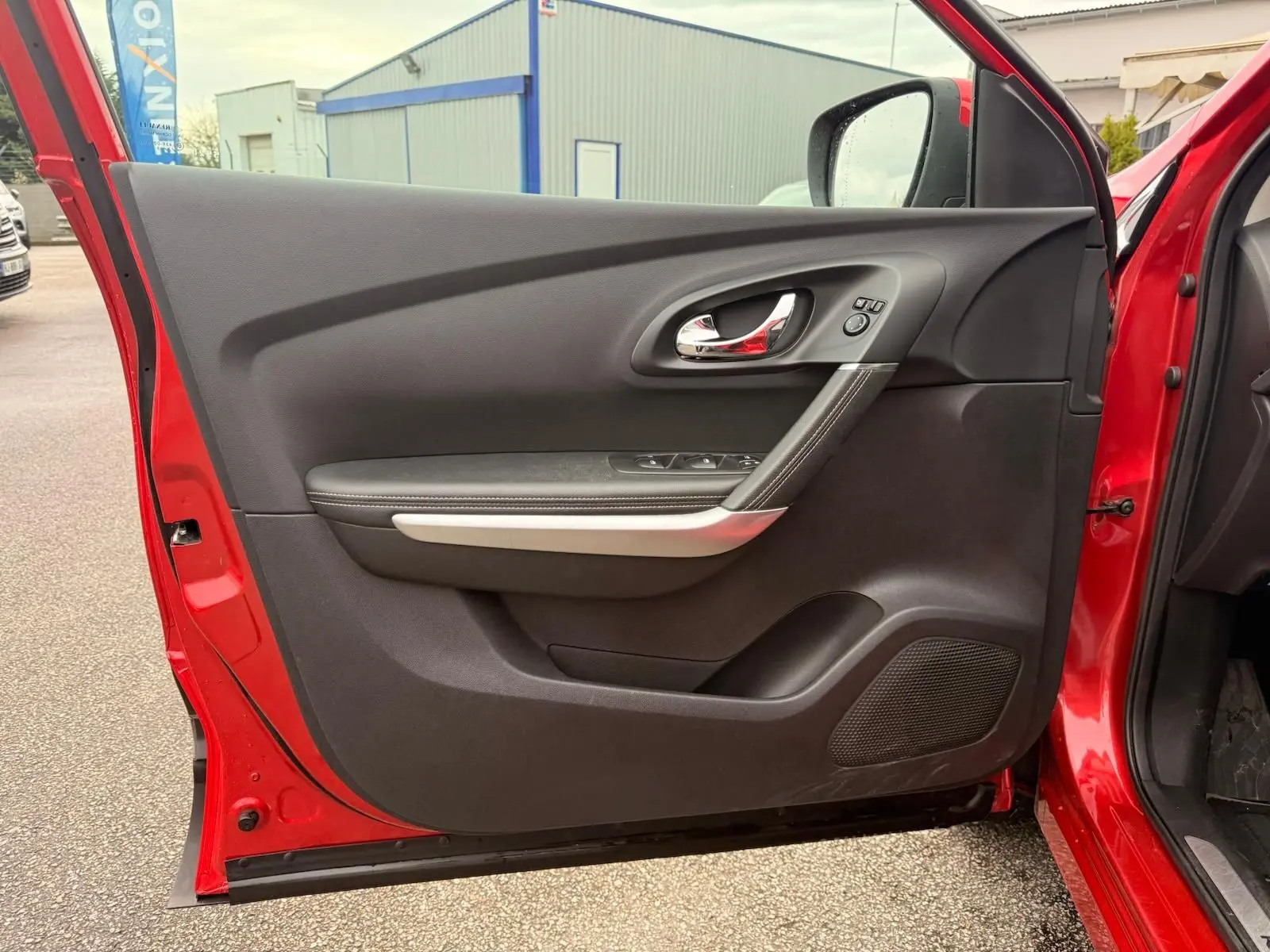 Vue intérieure de la porte avant gauche rouge flamme du Renault Kadjar 2016, avec poignée chrome et commandes électriques.