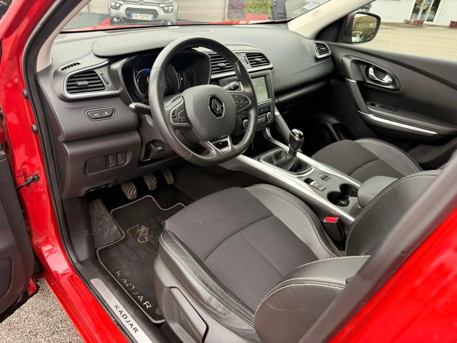 Vue intérieure côté conducteur du Renault Kadjar rouge flamme 2016, avec volant multifonctions et boîte manuelle.