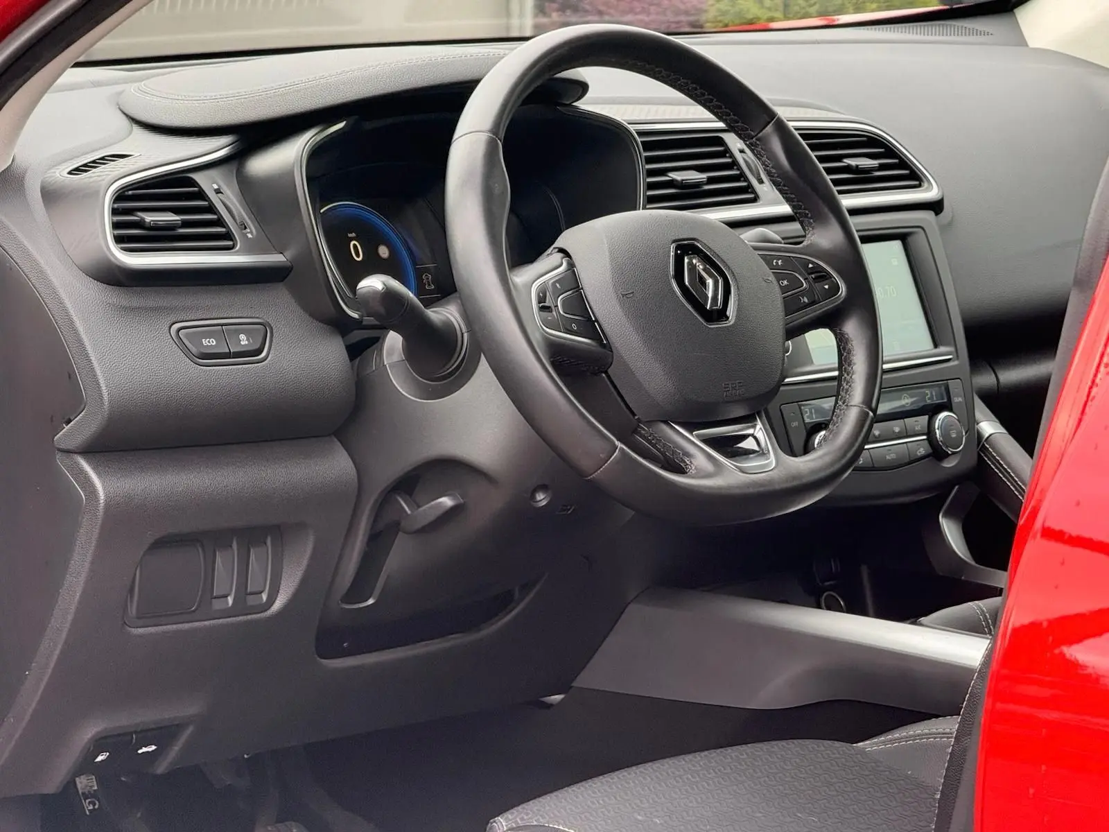 Vue intérieure côté conducteur du Renault Kadjar rouge flamme, mettant en valeur le volant et le tableau de bord digital.