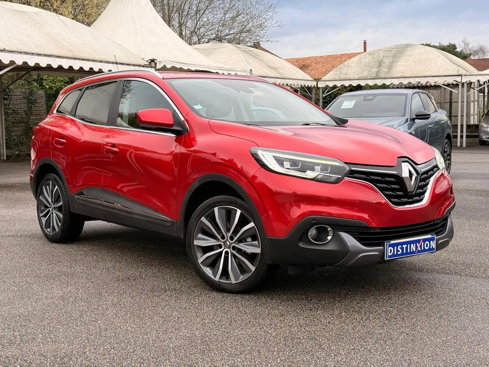 Renault Kadjar rouge flamme en 3/4 avant droit, avec jantes alliage bi-ton et calandre noire distinctive.