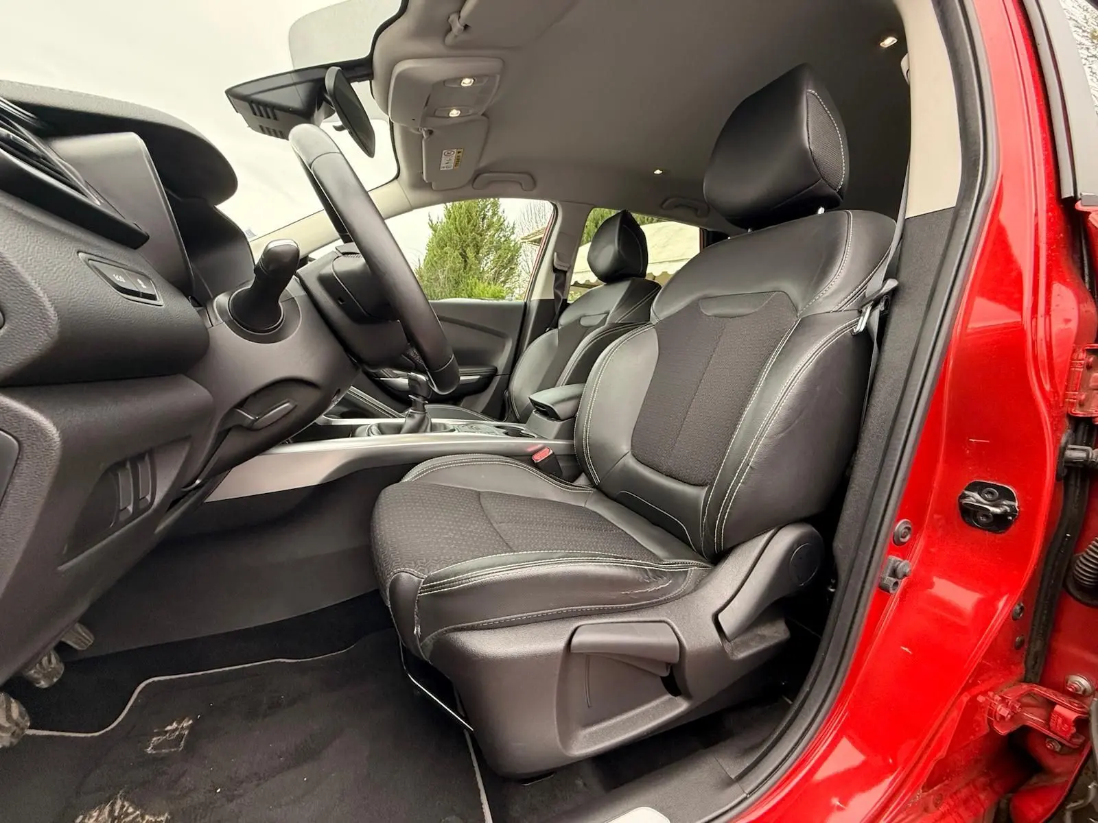 Vue intérieure côté conducteur du Renault Kadjar rouge flamme, mettant en valeur les sièges en cuir noir et la console centrale.