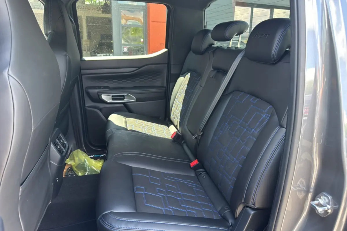 Vue côté droit de l'intérieur arrière du Ford Ranger 3.0 V6 gris carbone, sièges noirs avec surpiqûres bleues et motifs géométriques.