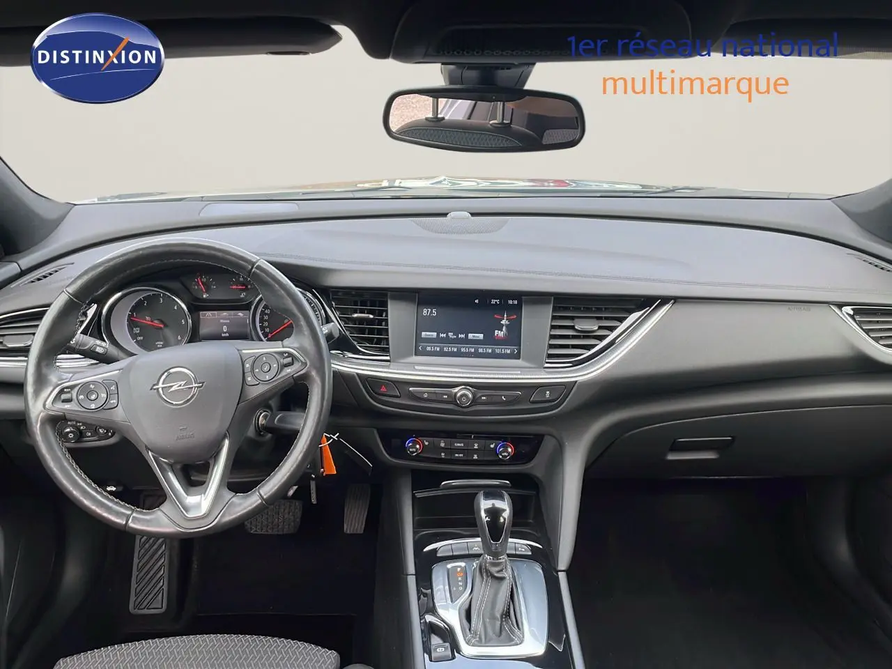 Vue intérieure de face du tableau de bord et volant d'une Opel Insignia Sports Tourer gris acier satinée, avec écran central et boîte automatique.