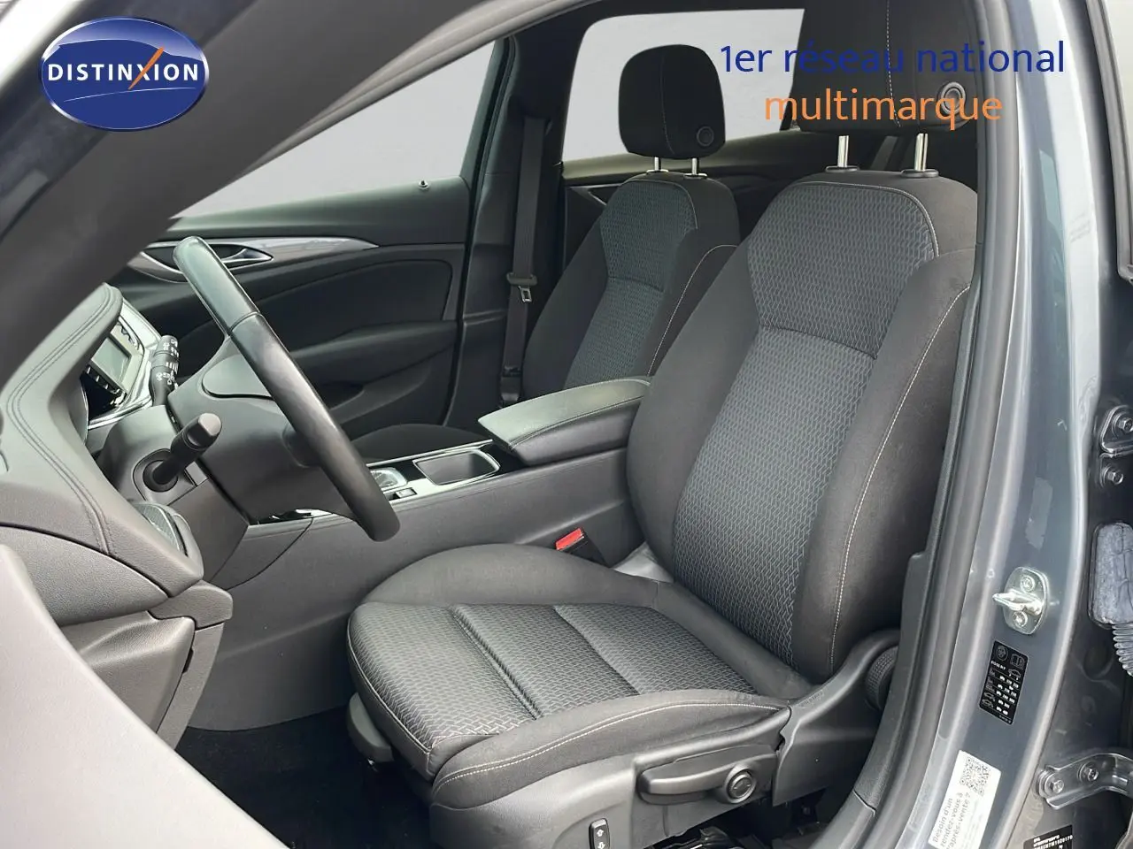 Vue intérieure côté conducteur de l’Opel Insignia Sports Tourer 2021, sièges tissu gris et portière gris acier satiné ouverte.