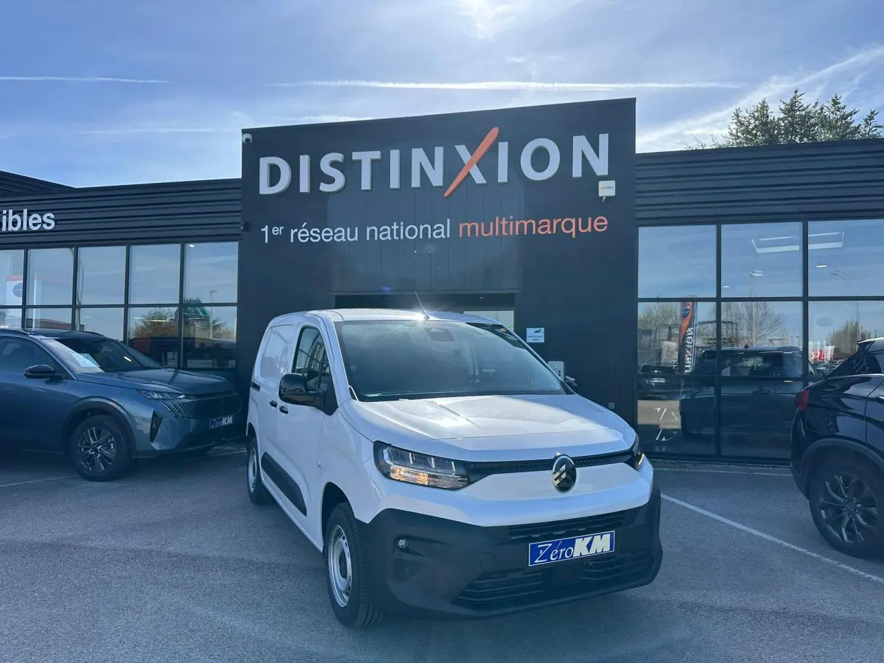 Vue 3/4 avant d'un Citroën Berlingo blanc Icy avec calandre noire, stationné devant un showroom Distinxion.