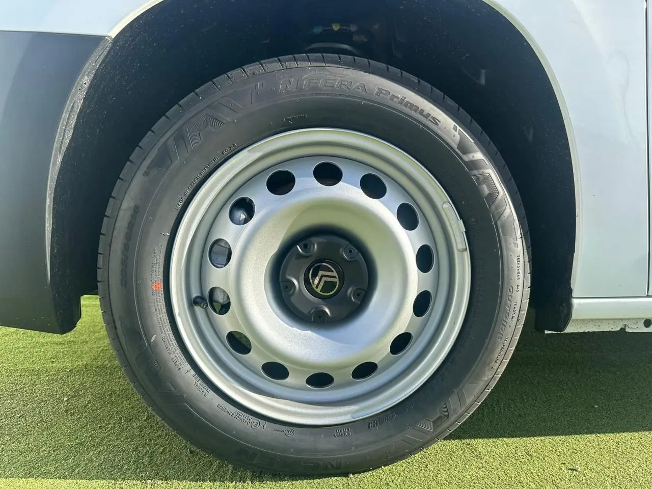 Gros plan sur la roue avant gauche en jante tôle grise du Citroën Berlingo blanc Icy, avec pneu noir visible.