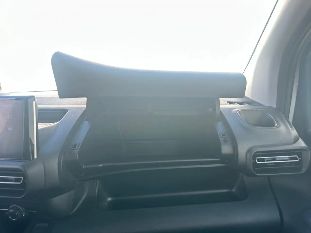 Vue intérieure du tableau de bord du Citroën Berlingo blanc, boîte à gants ouverte avec écran tactile visible à gauche.