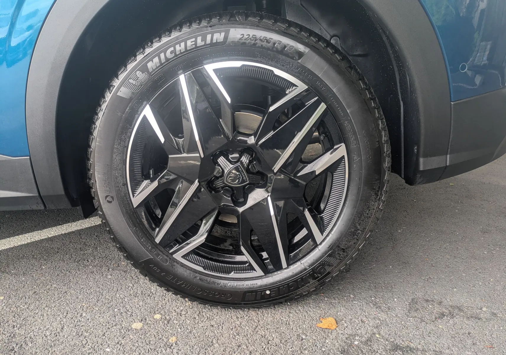 Gros plan sur la roue avant droite du Peugeot 3008 Hybrid bleu Obsession avec jante noire brillante et logo lion.