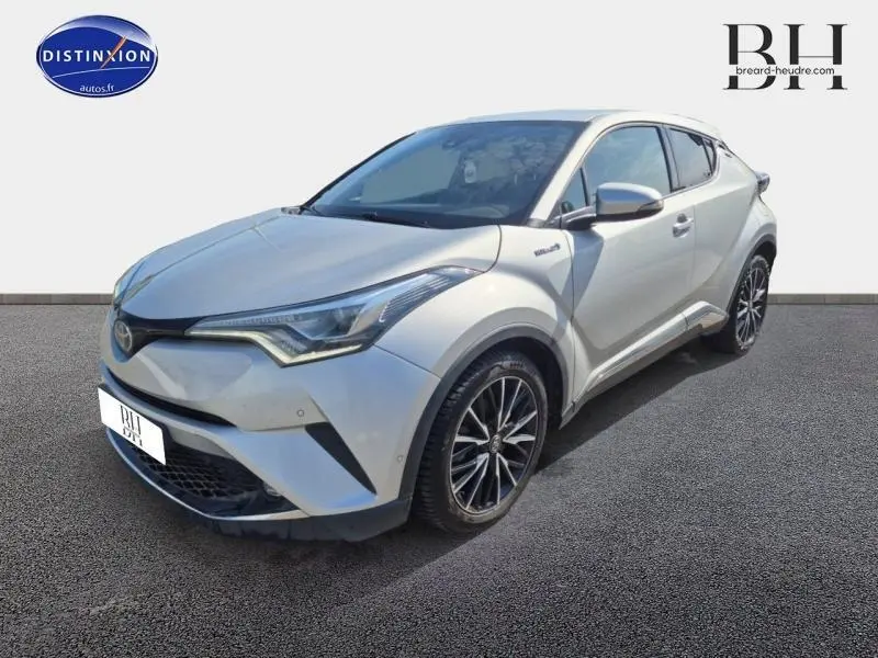 Toyota C-HR gris aluminium vu en 3/4 avant droit, avec jantes alliage et lignes anguleuses distinctives.