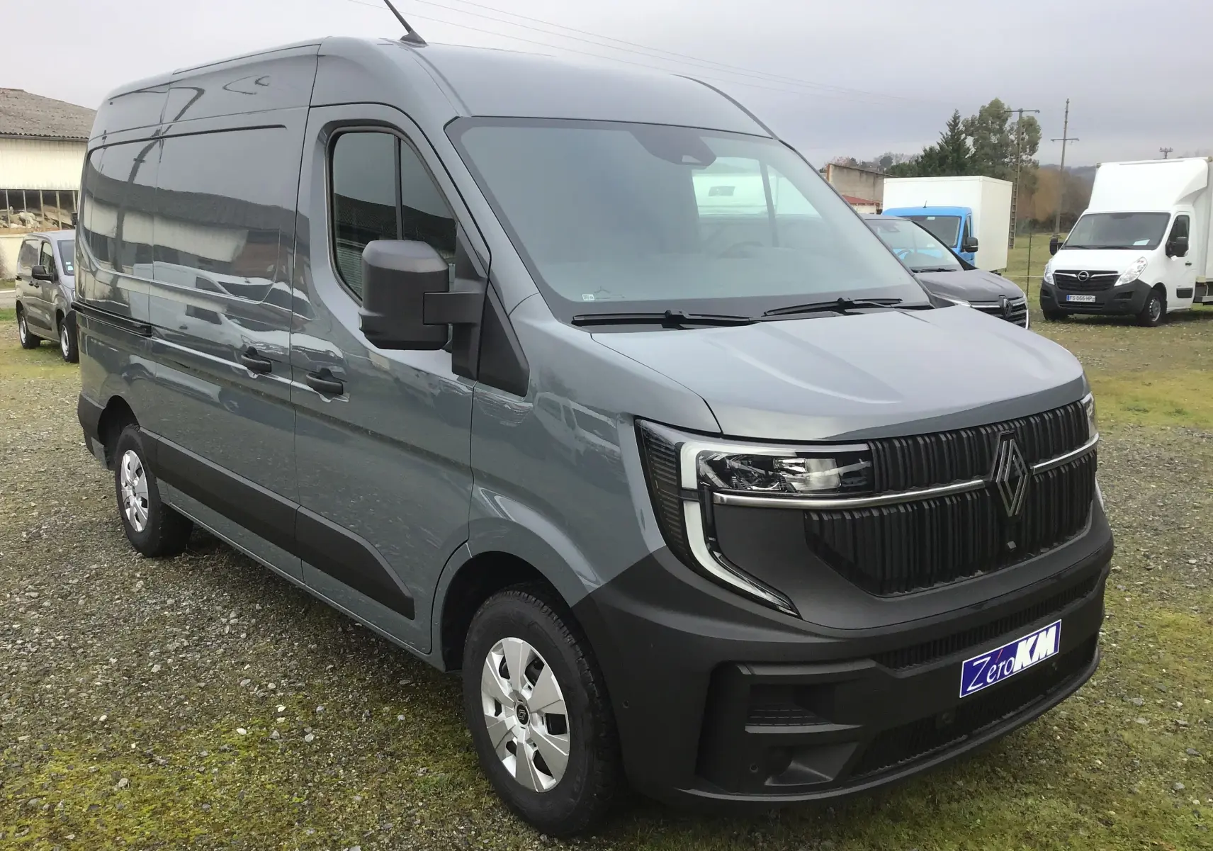 Vue 3/4 avant d’un Renault Master L2H2 gris urbain avec calandre noire et pare-chocs noir mat sur un terrain extérieur.