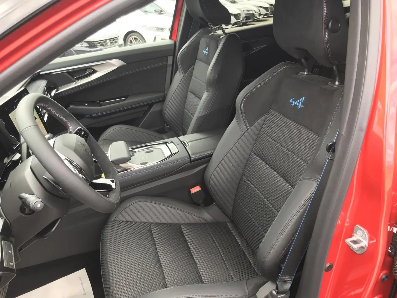 Vue intérieure côté conducteur du Renault Austral 2025 rouge noir, sièges sport Esprit Alpine avec surpiqûres bleues et logo brodé.