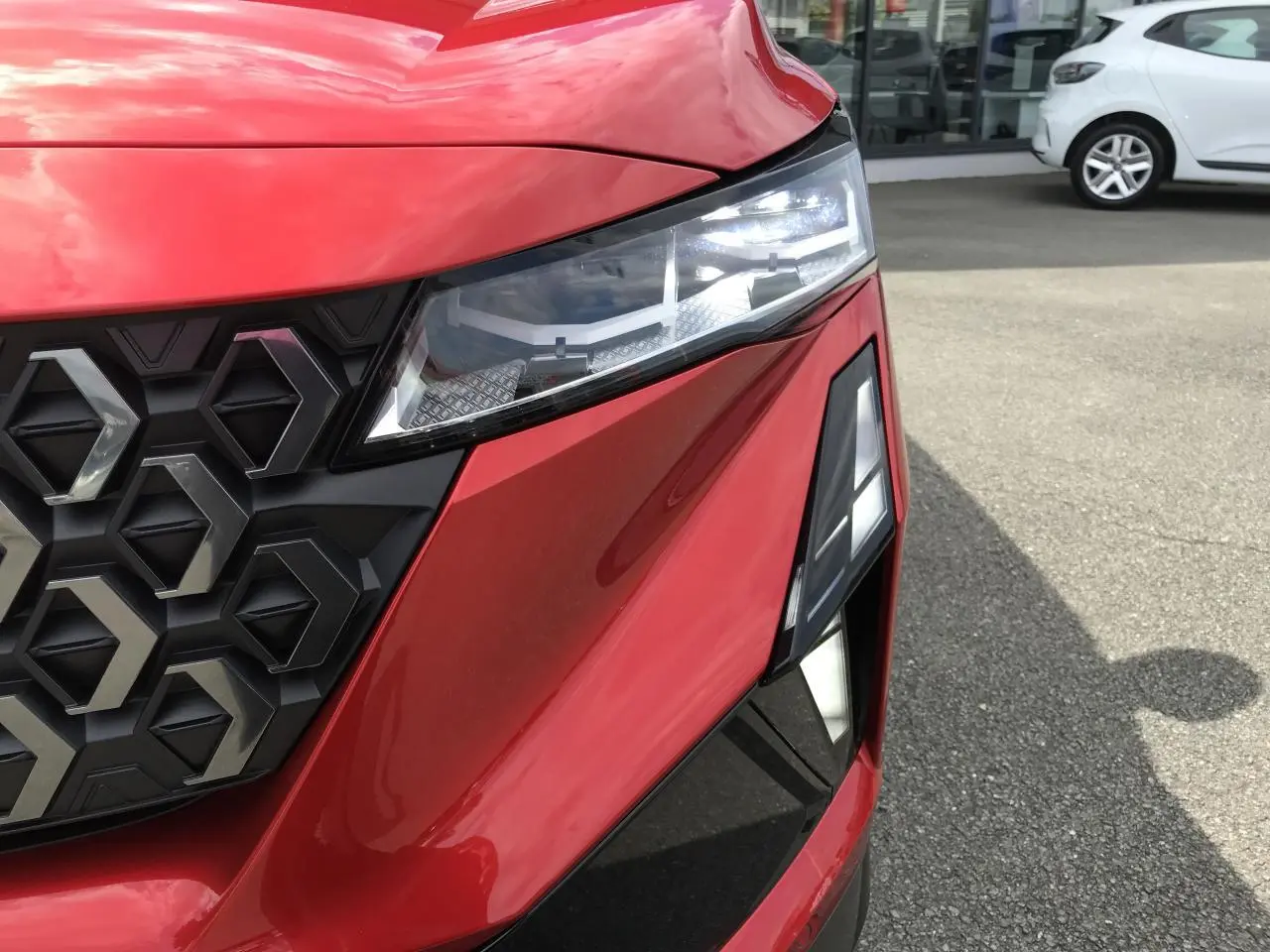 Gros plan sur l'avant droit rouge et noir du Renault Austral 2025, mettant en valeur le phare LED et la calandre hexagonale.