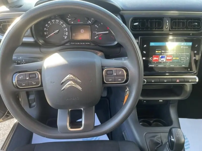 Vue intérieure centrée sur le volant et le tableau de bord d'une Citroën C3 gris foncé, avec écran tactile et boîte manuelle.