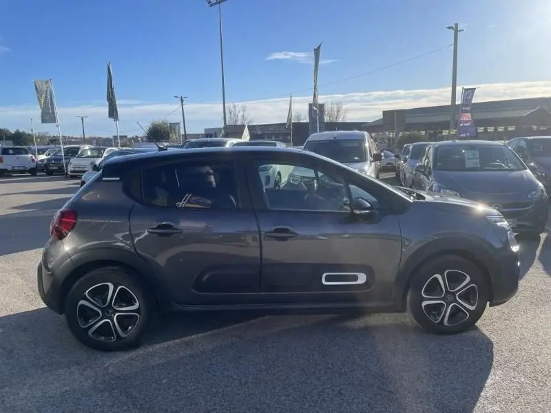 Vue de profil côté gauche d'une Citroën C3 gris foncé 2021 avec jantes distinctives et inserts blancs sur les portes.