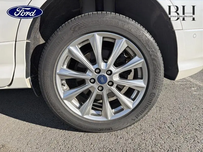 Gros plan sur la roue avant droite avec jante alu argentée du Ford Kuga blanc Premium Platinum de 2017.