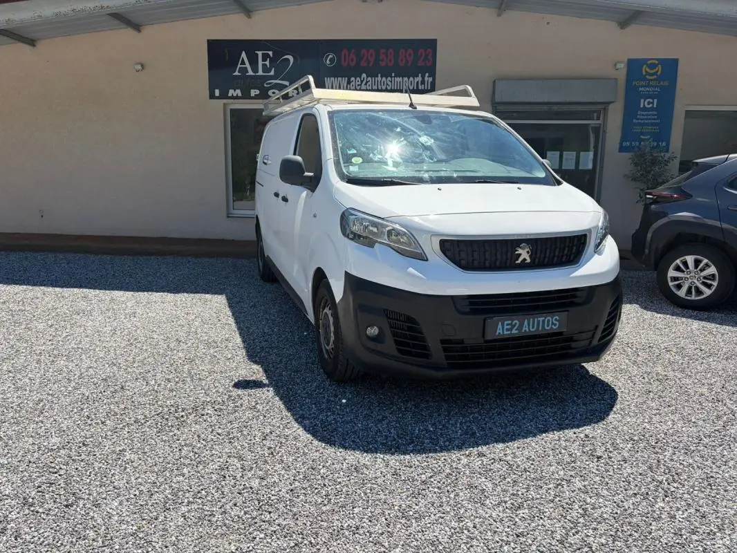 Peugeot Expert Fourgon blanc en 3/4 avant droit avec galerie de toit, stationné devant un bâtiment commercial.