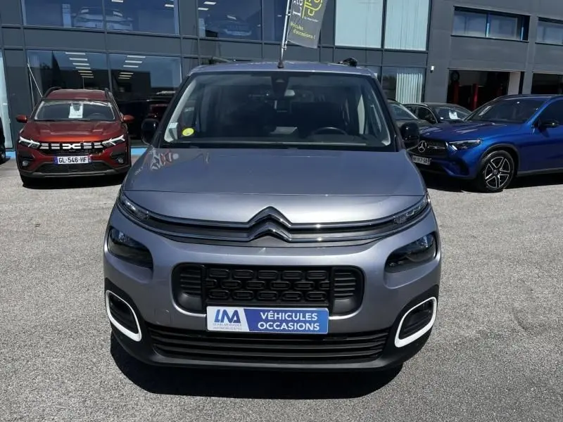 Vue avant d'un Citroën Berlingo XL gris métal 2021, avec calandre noire et phares distinctifs, stationné devant un showroom.