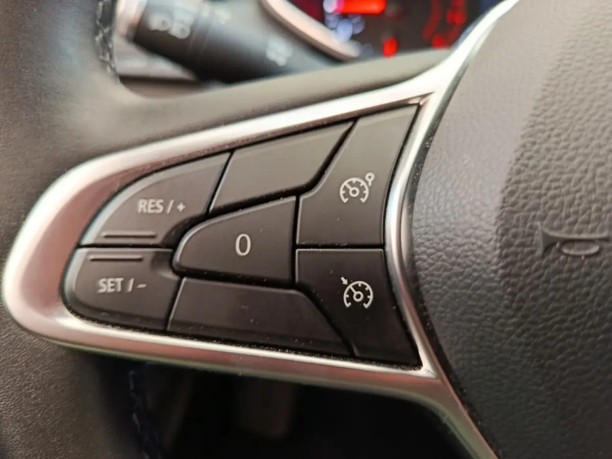 Gros plan sur les commandes du régulateur de vitesse au volant cuir synthétique d’une Renault Clio Business gris clair.