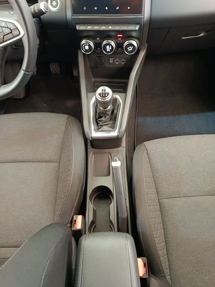 Vue intérieure centrée sur la console centrale d'une Renault Clio Business gris clair avec levier de vitesse manuel et sièges tissu noirs.