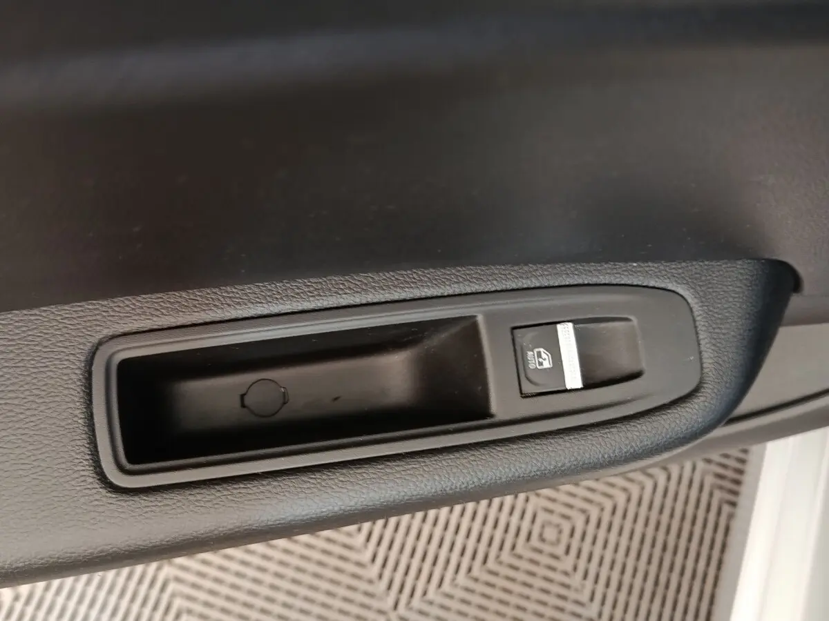 Gros plan sur le bouton de verrouillage centralisé noir dans l'accoudoir intérieur d'une Renault Clio gris clair.