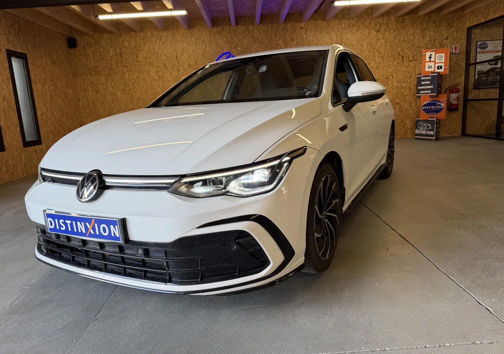 Volkswagen Golf 2.0 TDI 150 DSG7 R-Line blanc vue 3/4 avant en intérieur avec jantes noires et phares allumés.