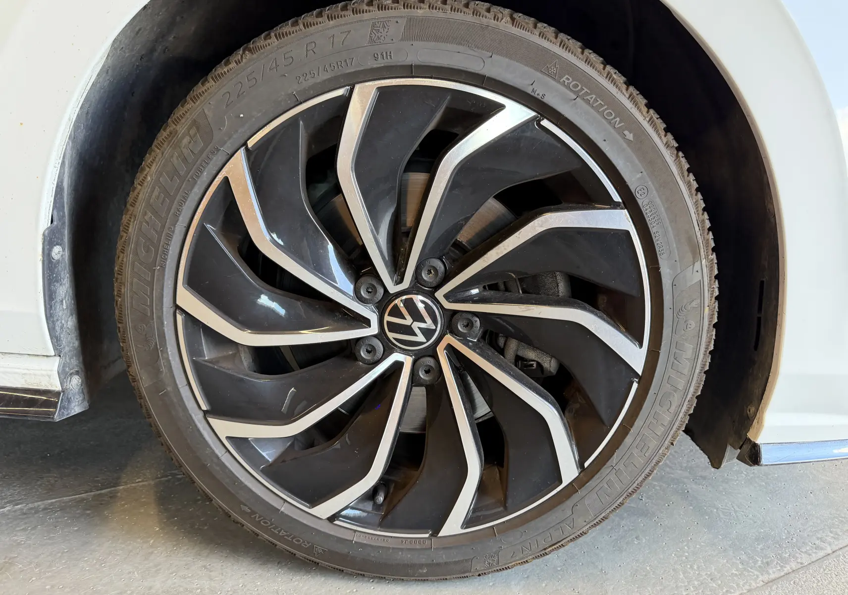 Gros plan sur la roue avant gauche d'une Volkswagen Golf blanche 2023 avec jante alliage noire et argentée R-Line.
