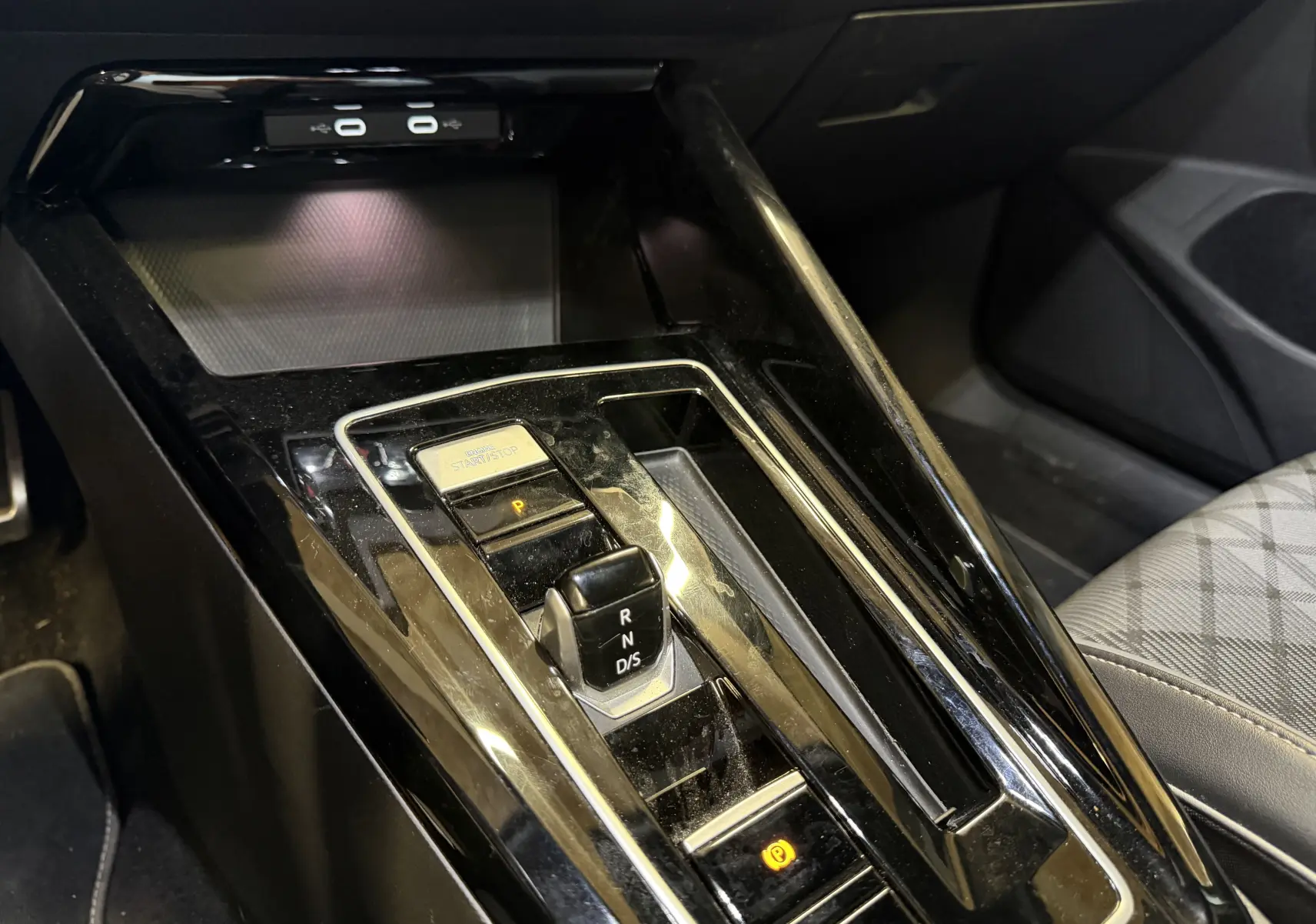 Vue rapprochée de la console centrale noire brillante avec levier de vitesses DSG et bouton start/stop dans une Volkswagen Golf blanche.