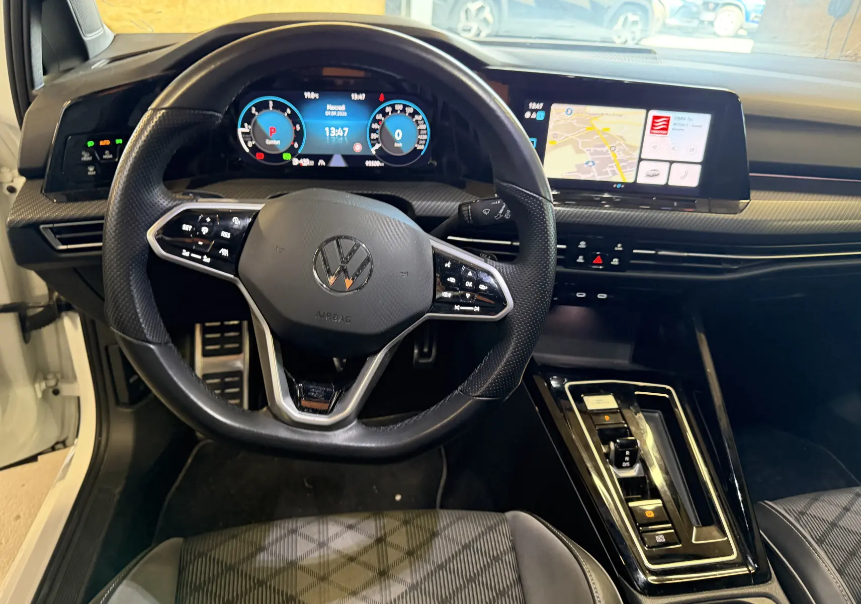 Vue intérieure centrée sur le volant noir et le tableau de bord digital d'une Volkswagen Golf 2.0 TDI blanche de 2023.