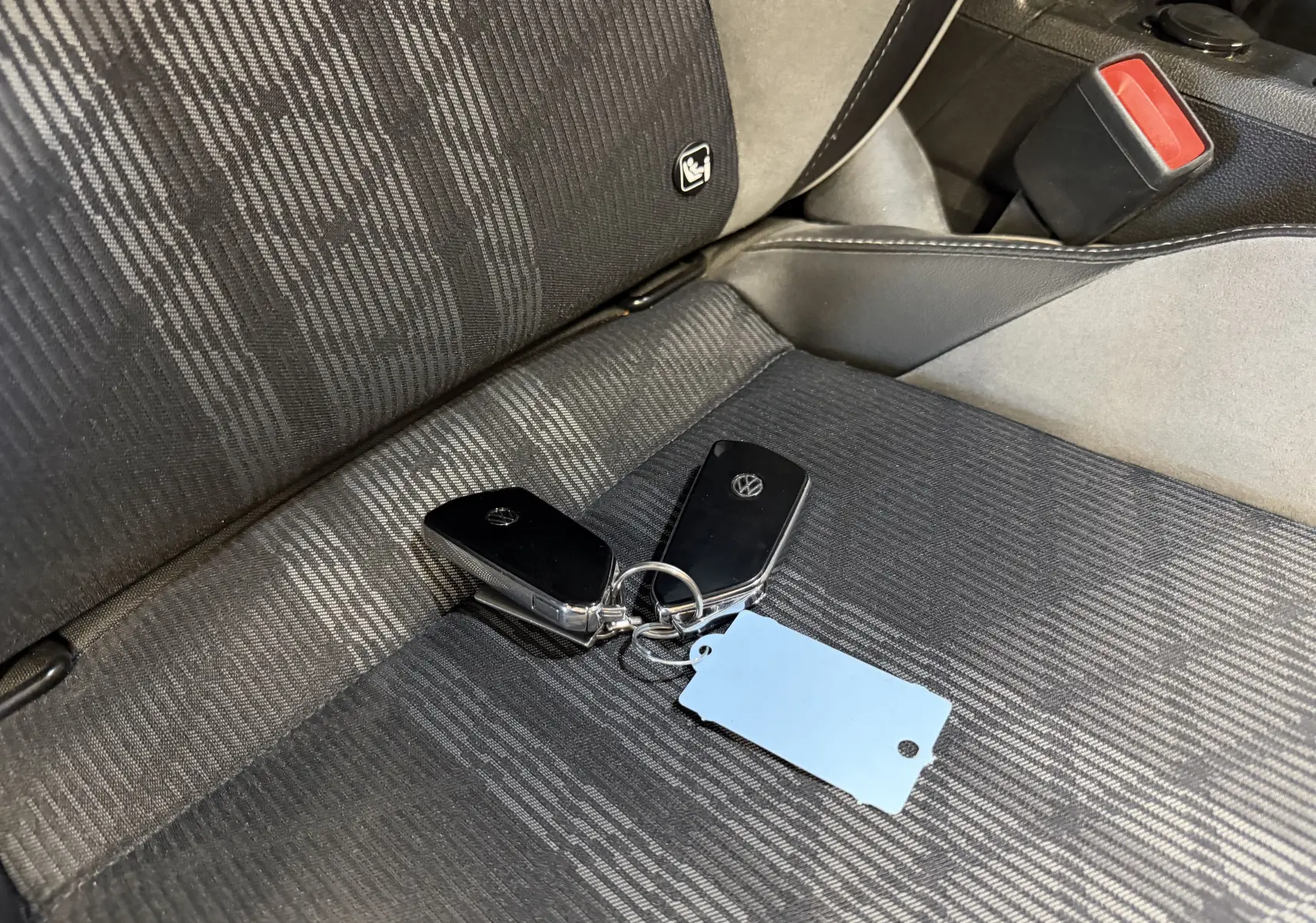 Gros plan sur les clés noires Volkswagen posées sur le siège tissu gris foncé à motifs du conducteur.