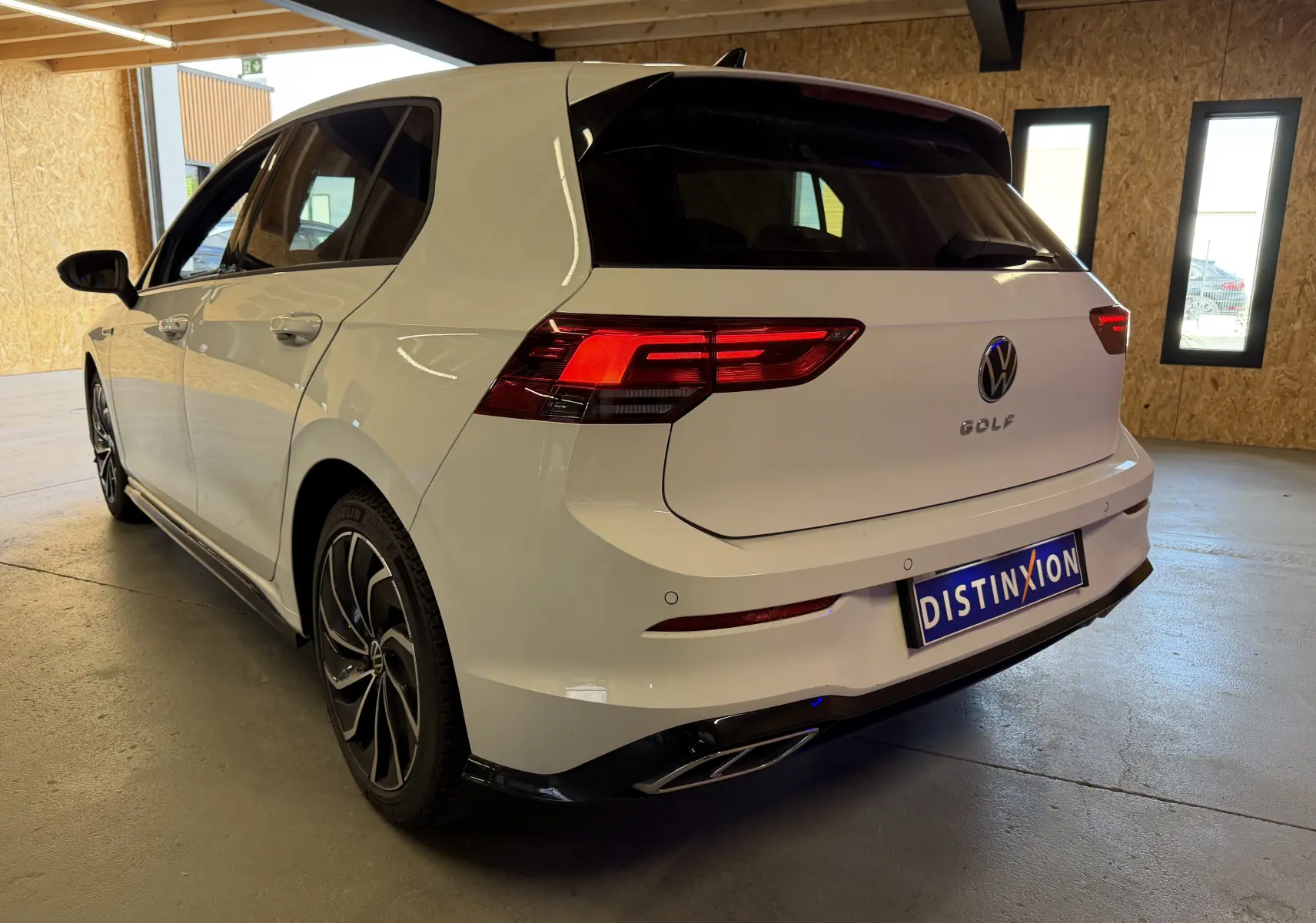 Vue 3/4 arrière droite d'une Volkswagen Golf 2.0 TDI 150 DSG7 R-Line blanche avec feux arrière LED et jantes noires en intérieur.