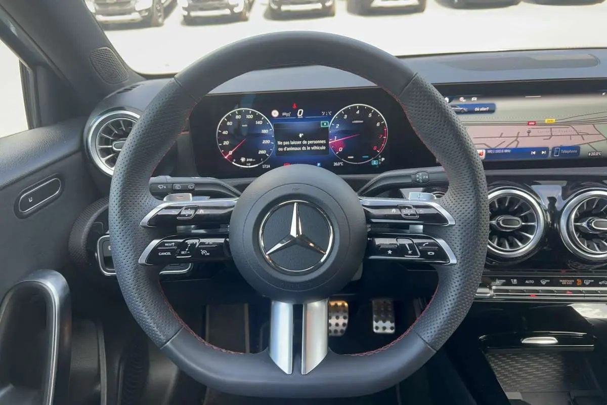 Vue intérieure centrée sur le volant cuir perforé AMG de la Mercedes Classe A 200 7G-DCT avec tableau de bord digital et aérateurs ronds.
