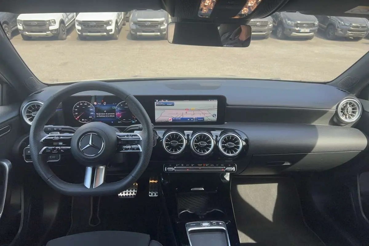 Vue intérieure avant de la Mercedes Classe A 200 AMG Line 2025, tableau de bord noir avec écran digital et aérateurs ronds chromés.